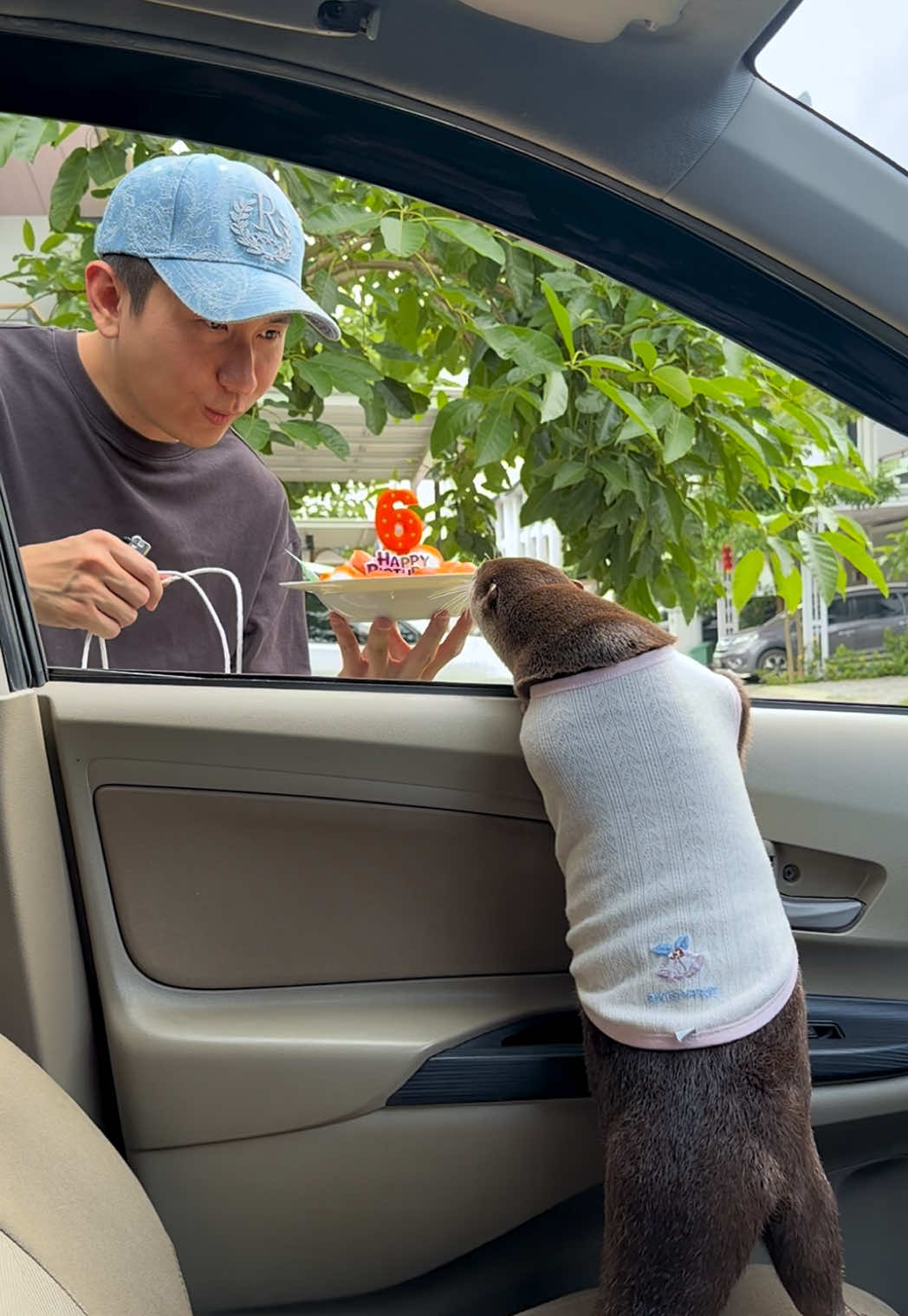 Degen the otter leaning toward a man holding a birthday cake with a number six candle