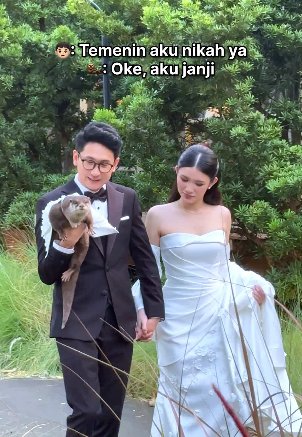 Wedding photo of a bride and groom holding Degen the otter dressed in formal wear